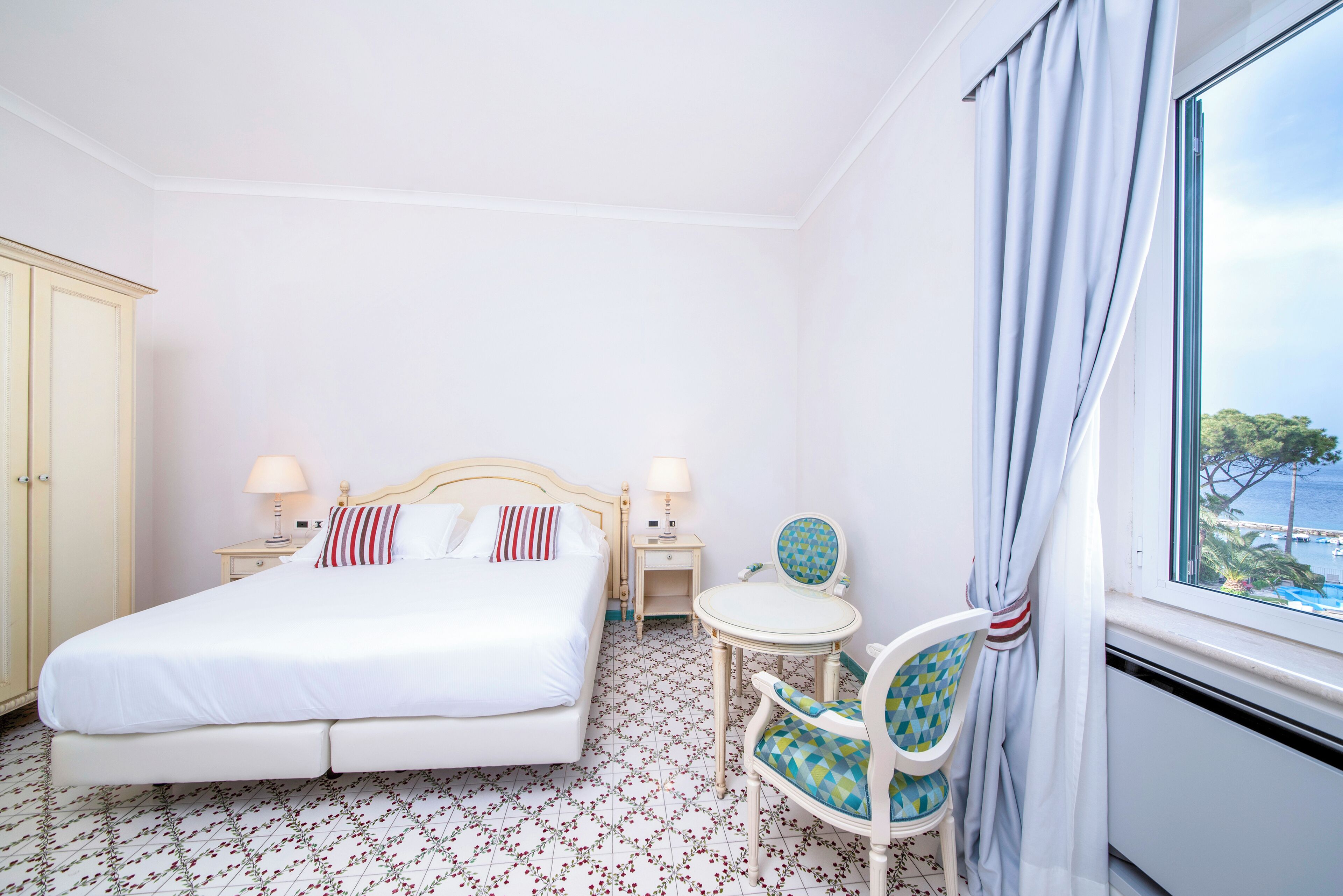 Een hotelkamer met een bed, nachtkastjes, een stoel, een tafeltje en een raam met gordijnen.