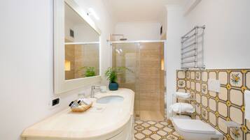 Uma casa de banho moderna com uma toucador curvo, uma cabine de duche com paredes de vidro e um chão em mosaico.
