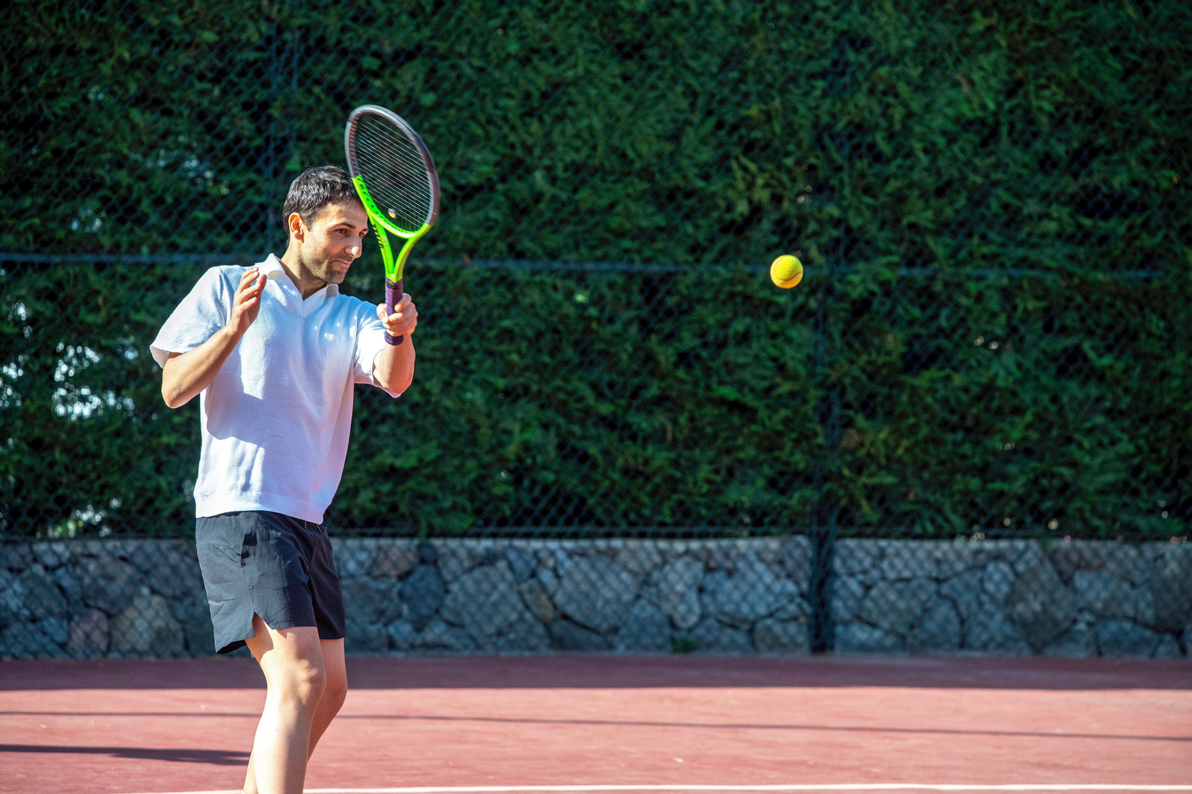 Un campo da tennis con un giocatore in camicia bianca e pantaloncini neri, che tiene in mano una racchetta da tennis.