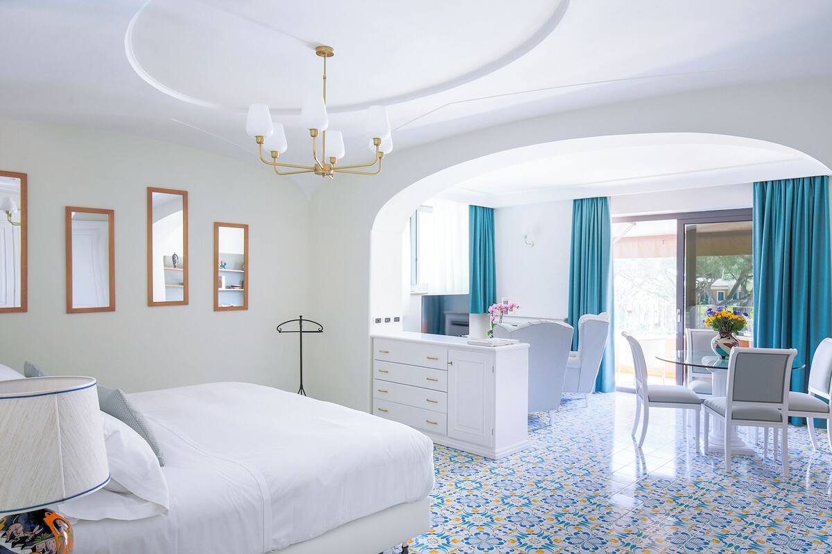 Une chambre d’hôtel avec un lit, un bureau, une chaise, un miroir et un lustre.