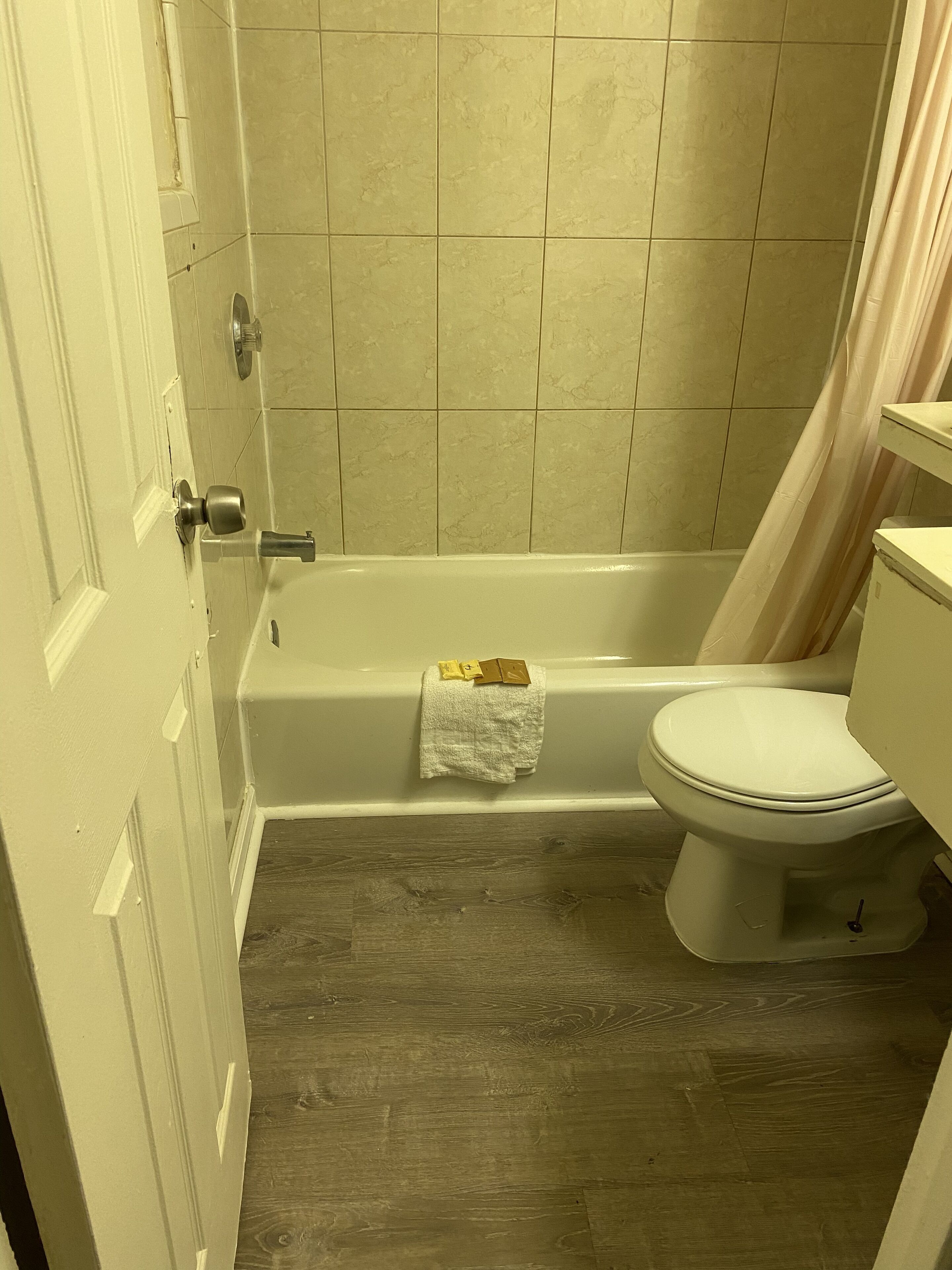 A bathroom with a bathtub, toilet, and wooden flooring.