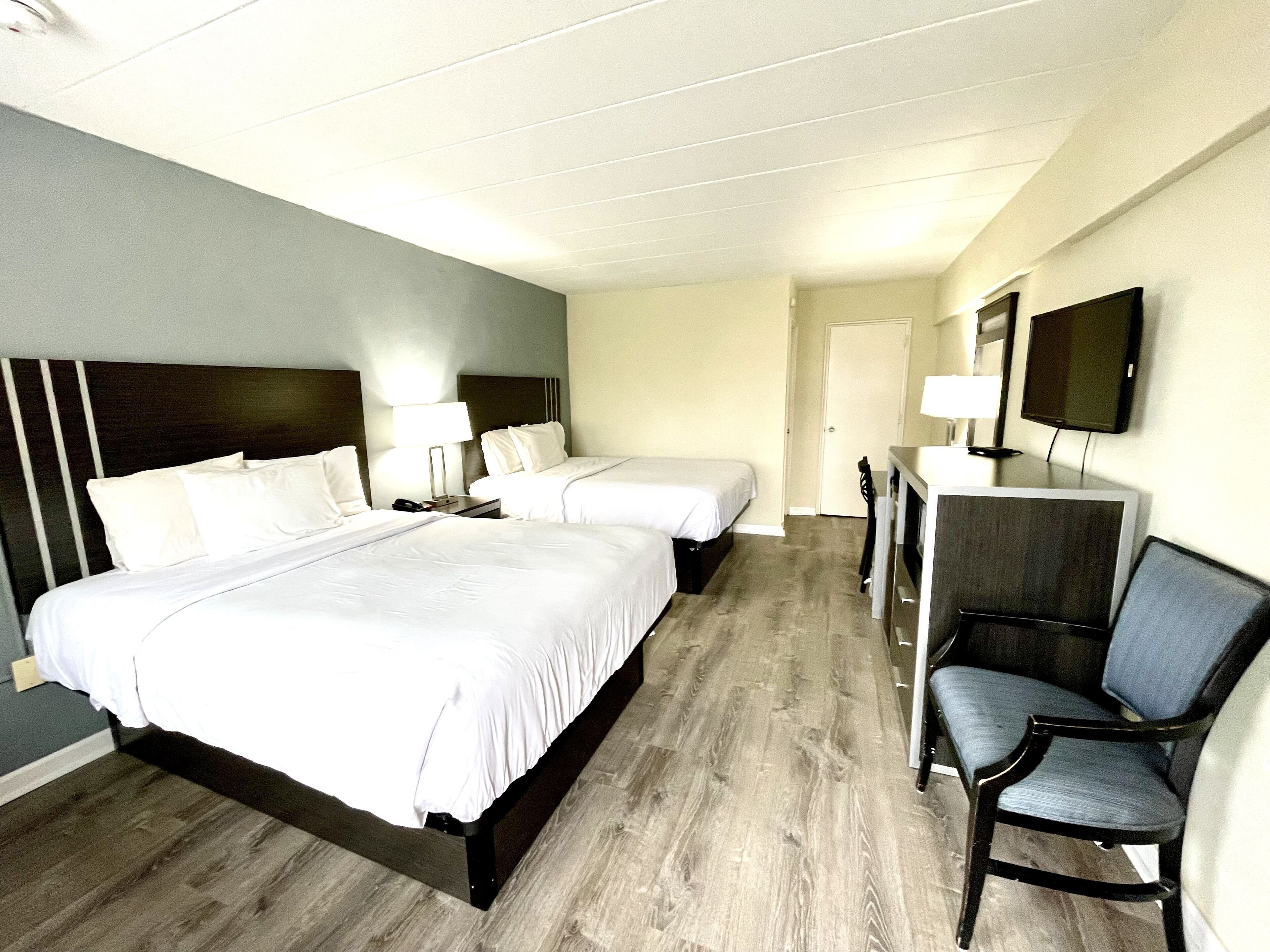 A hotel room with two beds, a desk with a chair, a television, and a door.