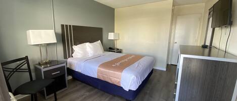 A hotel room with a bed, bedside tables, a desk, a chair, a lamp, and a TV.