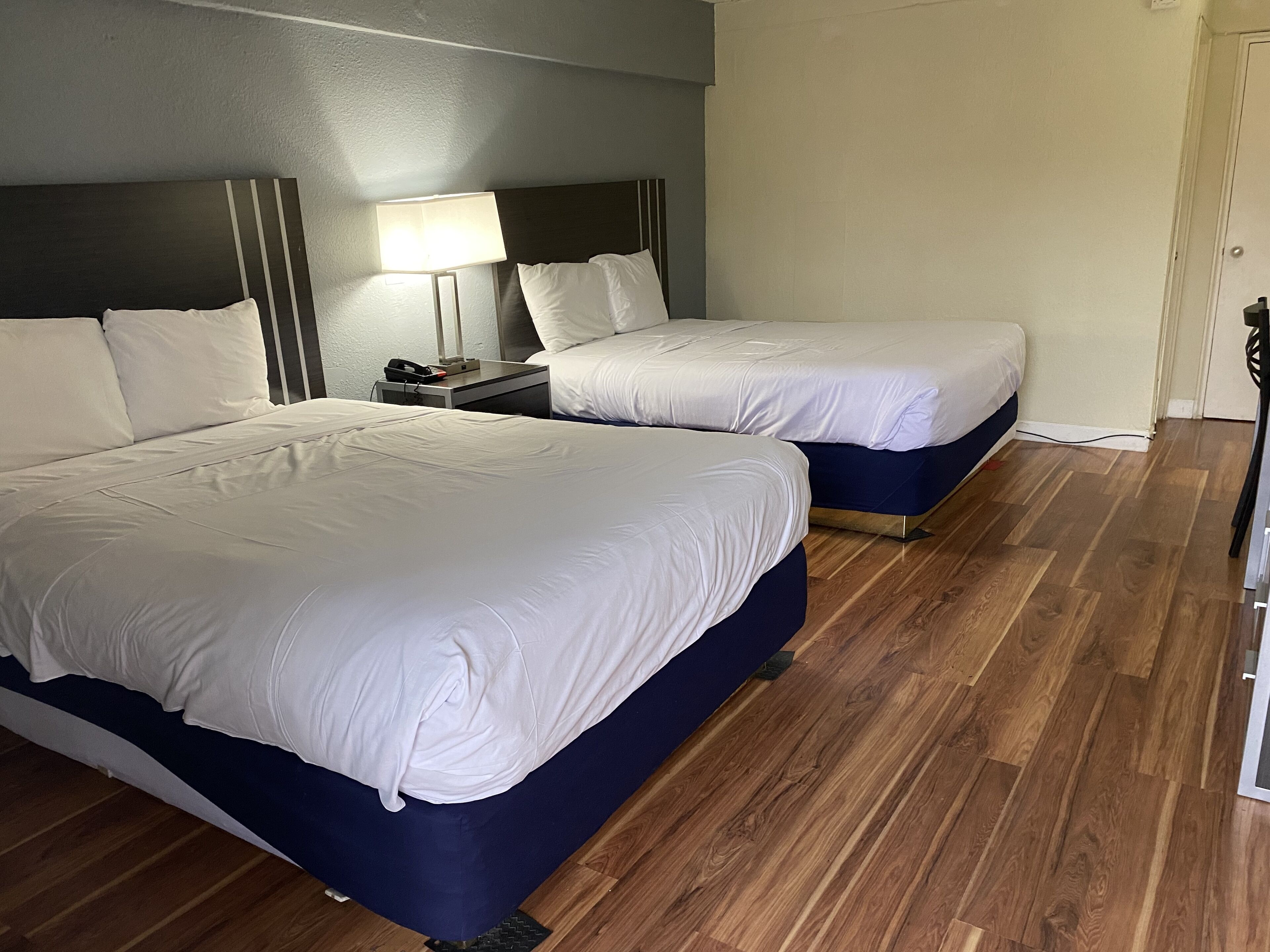 A hotel room with two beds, a nightstand with a lamp, and wooden flooring.