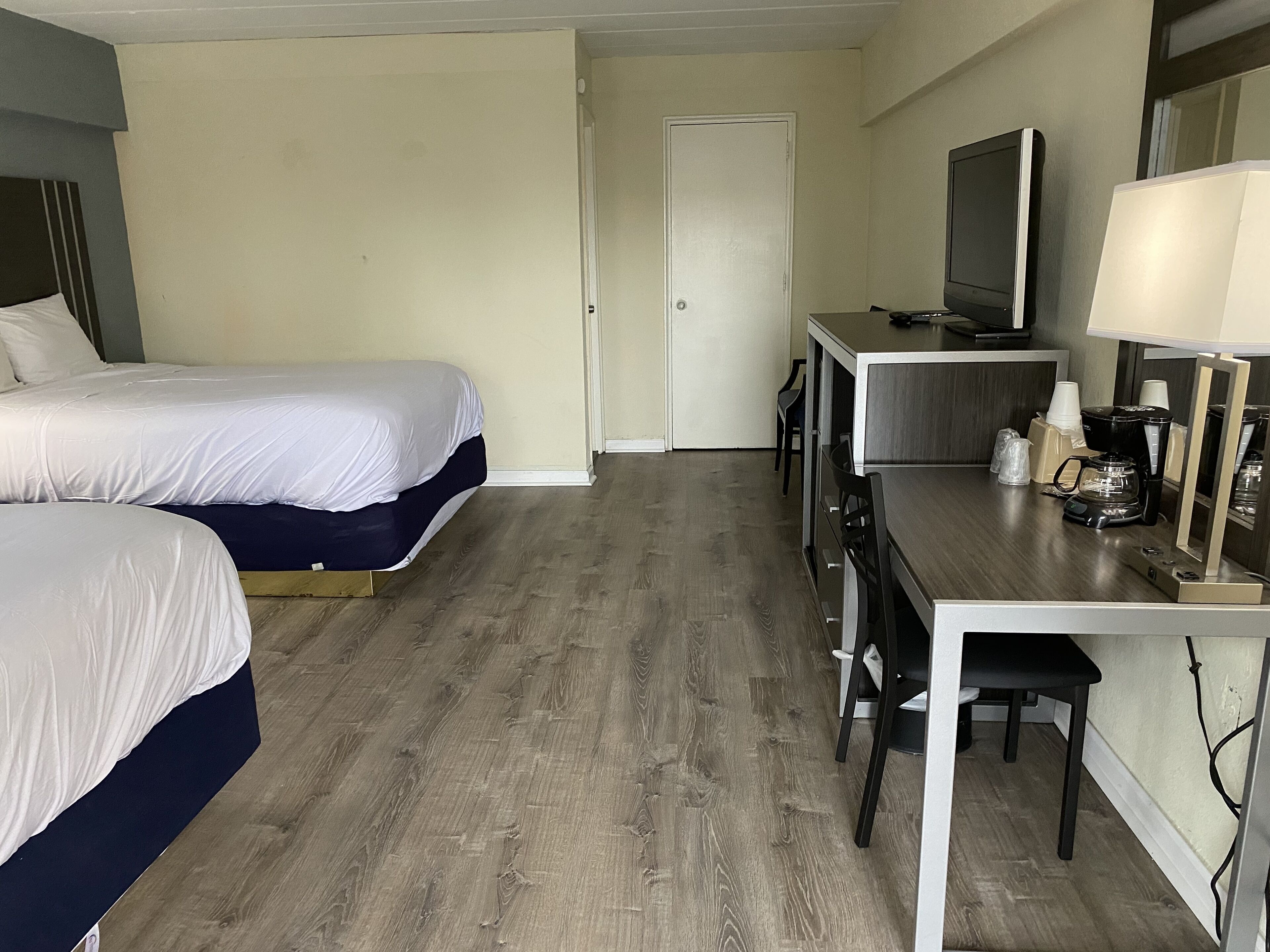 Quarto de hotel com duas camas, uma mesa com máquina de café, televisão e uma porta.