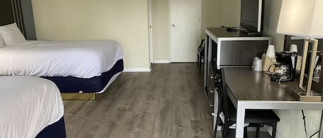Quarto de hotel com duas camas, uma mesa com máquina de café, televisão e uma porta.