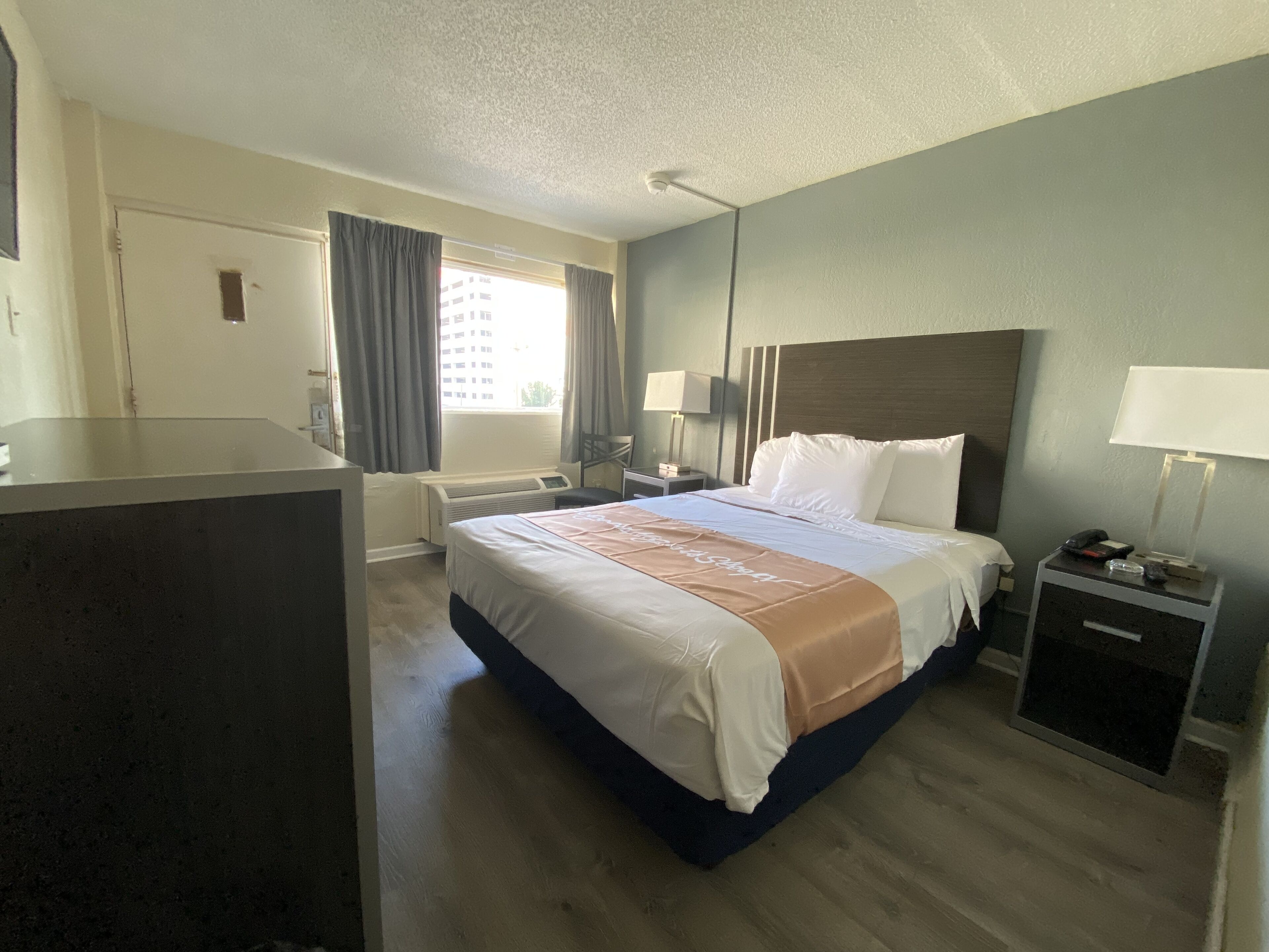 A hotel room with a bed, bedside tables, a desk, and a window with curtains.