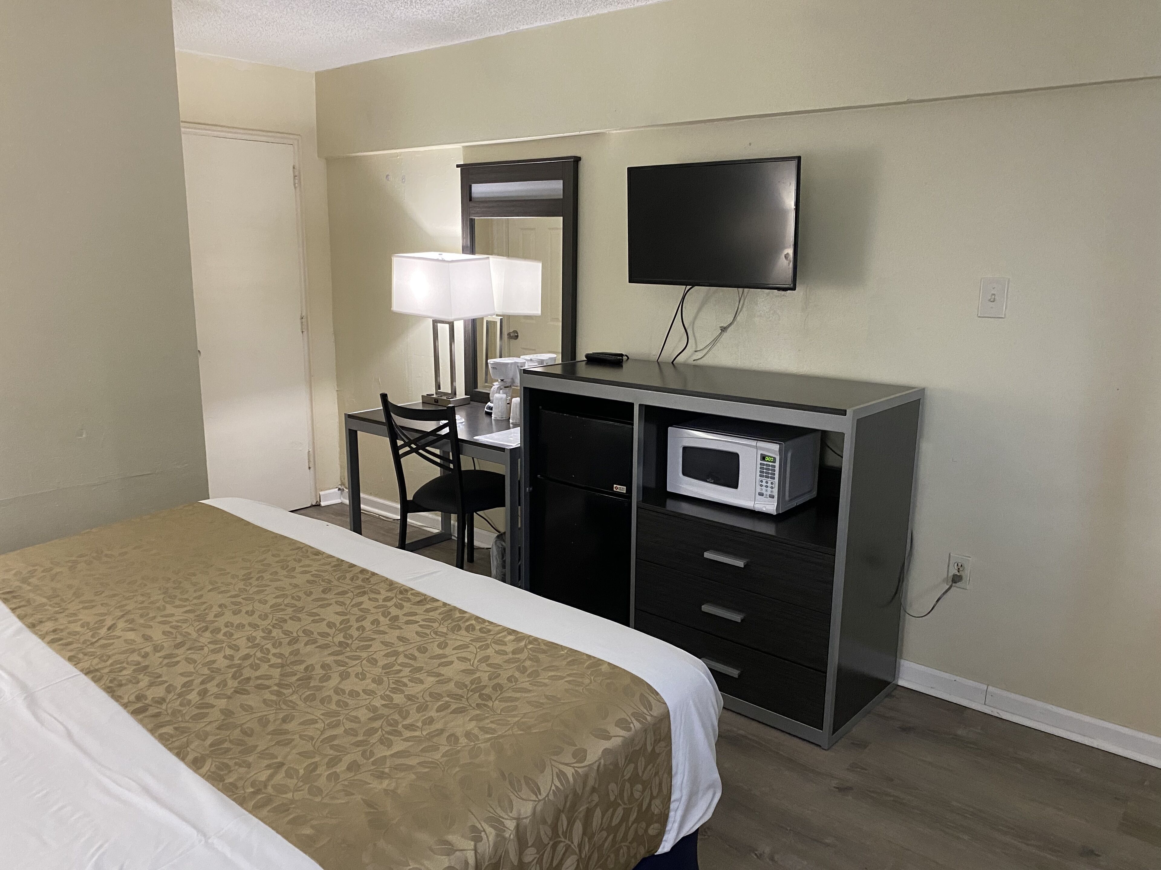 A hotel room with a bed, a desk with a lamp, a television, and a microwave.