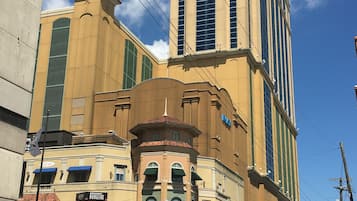 Un immeuble à plusieurs étages, doté d’une tour imposante, avec une entrée au niveau de la rue et une enseigne indiquant « Broadway Burgers », et une vue sur la rue avec des voitures et un passage piéton.