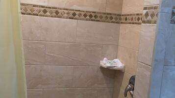 A shower area with beige tiles, a showerhead, and a small shelf with a towel.