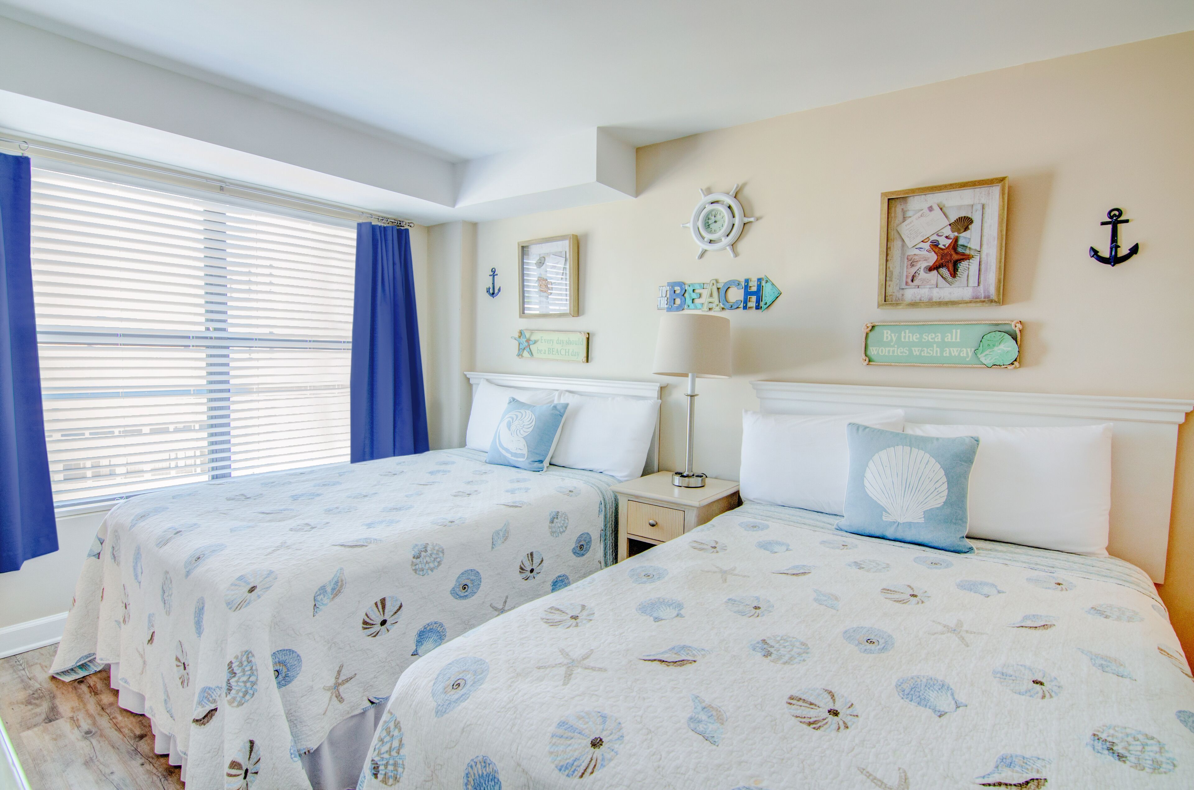Een slaapkamer met twee bedden, elk voorzien van een beddegoed met een nautisch thema, een nachtkastje, een lamp en wanddecoraties, waaronder een kompas en een anker.