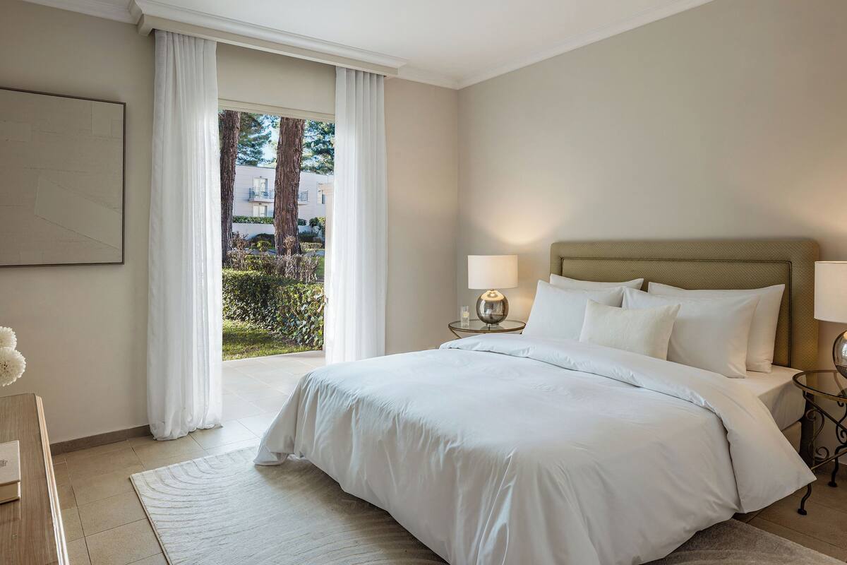 Ett hotellrum med en stor säng, två sängbord, utsikt över träd och byggnader utanför och en inramad tavla på väggen.