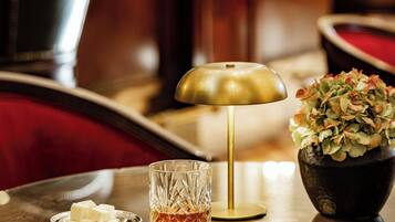 A table with a glass, a small dish of butter, a gold lamp, and a vase with flowers.