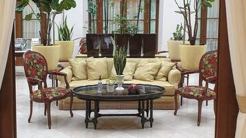 A spacious lobby with a beige sofa, floral chairs, a coffee table, and large potted plants.