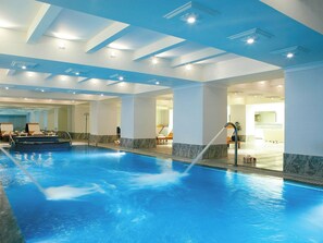 Une grande piscine intérieure dotée d’une fontaine, entourée d’un espace spacieux aménagé avec des sièges et un comptoir d’accueil.