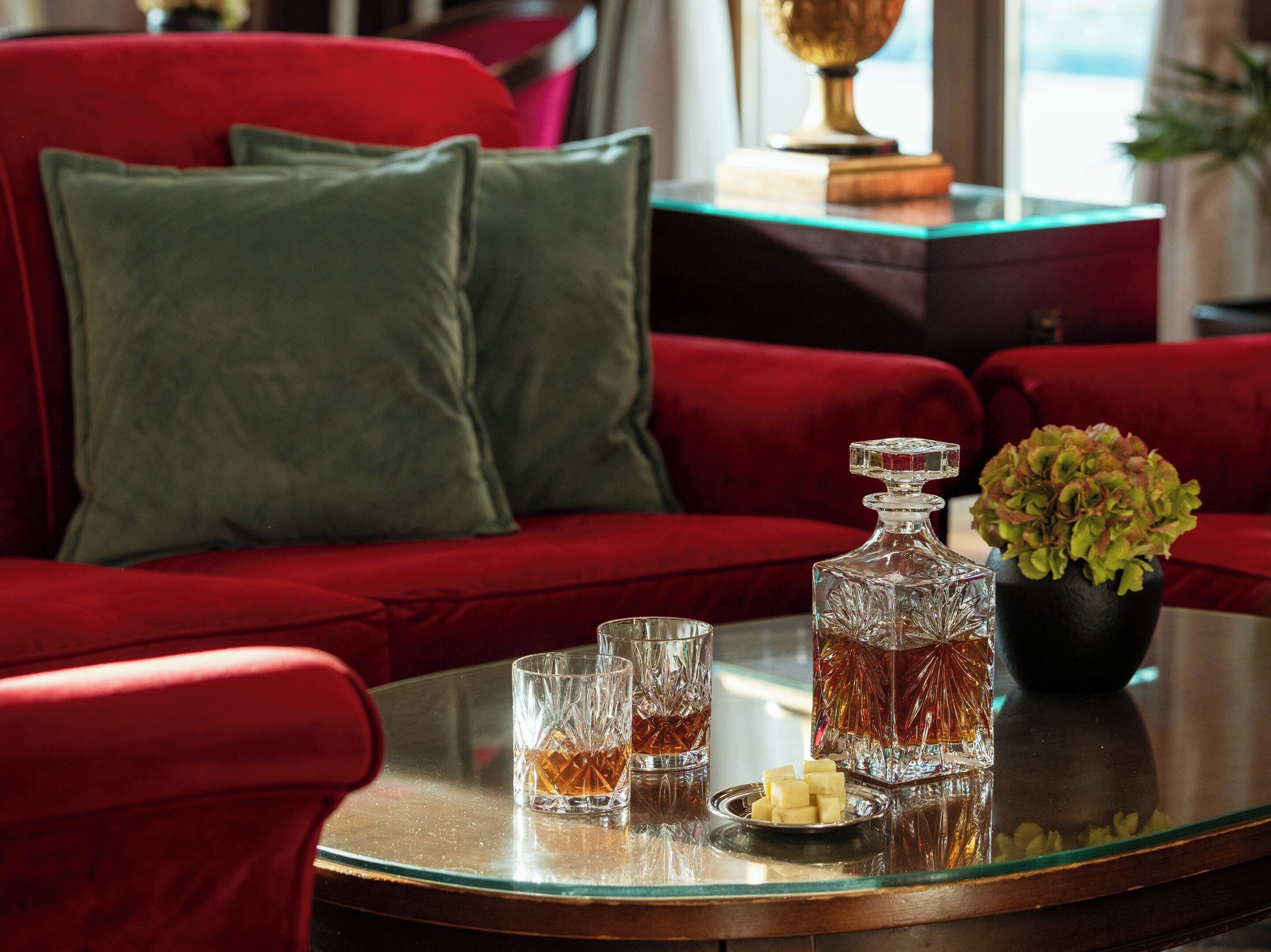 A red sofa with green cushions, a glass table with a decanter, glasses, and cubes of butter.