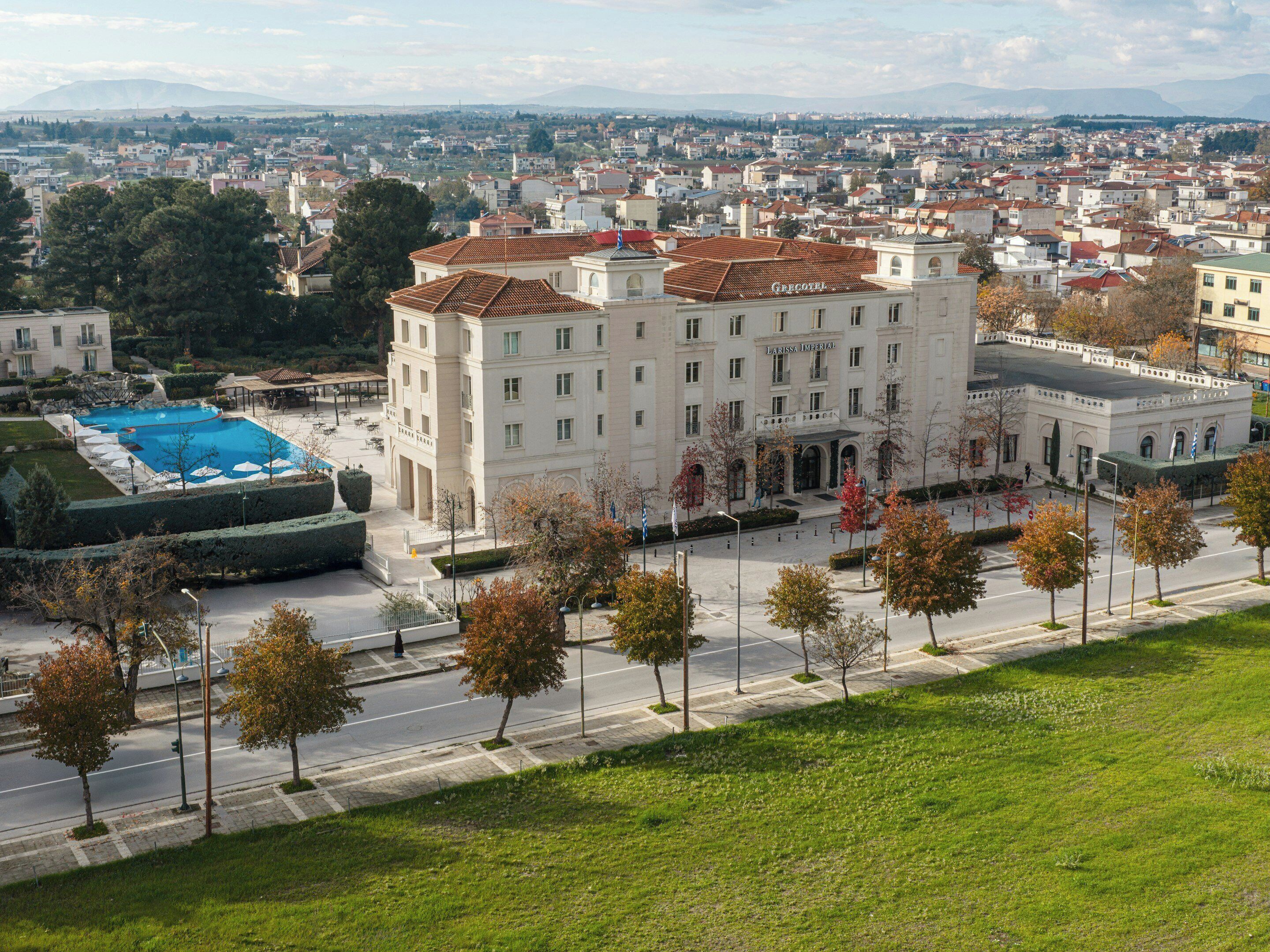 Un grand bâtiment doté d’une piscine, entouré d’arbres, avec une vue sur la ville en arrière-plan.