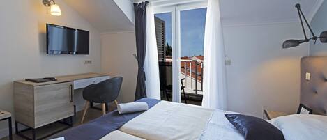 Habitación de hotel con cama, escritorio, silla, televisor y balcón con vistas a edificios.