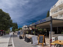 A hotel named "Hotel Perla" with outdoor seating and a signboard advertising a special offer on grilled fresh fish with vegetables.