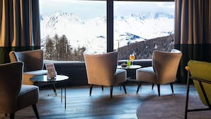 Une pièce avec vue sur des montagnes enneigées, deux fauteuils, une petite table avec une boisson et un menu posé sur la table.