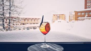 Ein Glas rotes Getränk mit Trinkhalm auf einer Untertasse, aufgenommen durch ein Fenster mit verschneiter Landschaft und Gebäuden im Hintergrund.