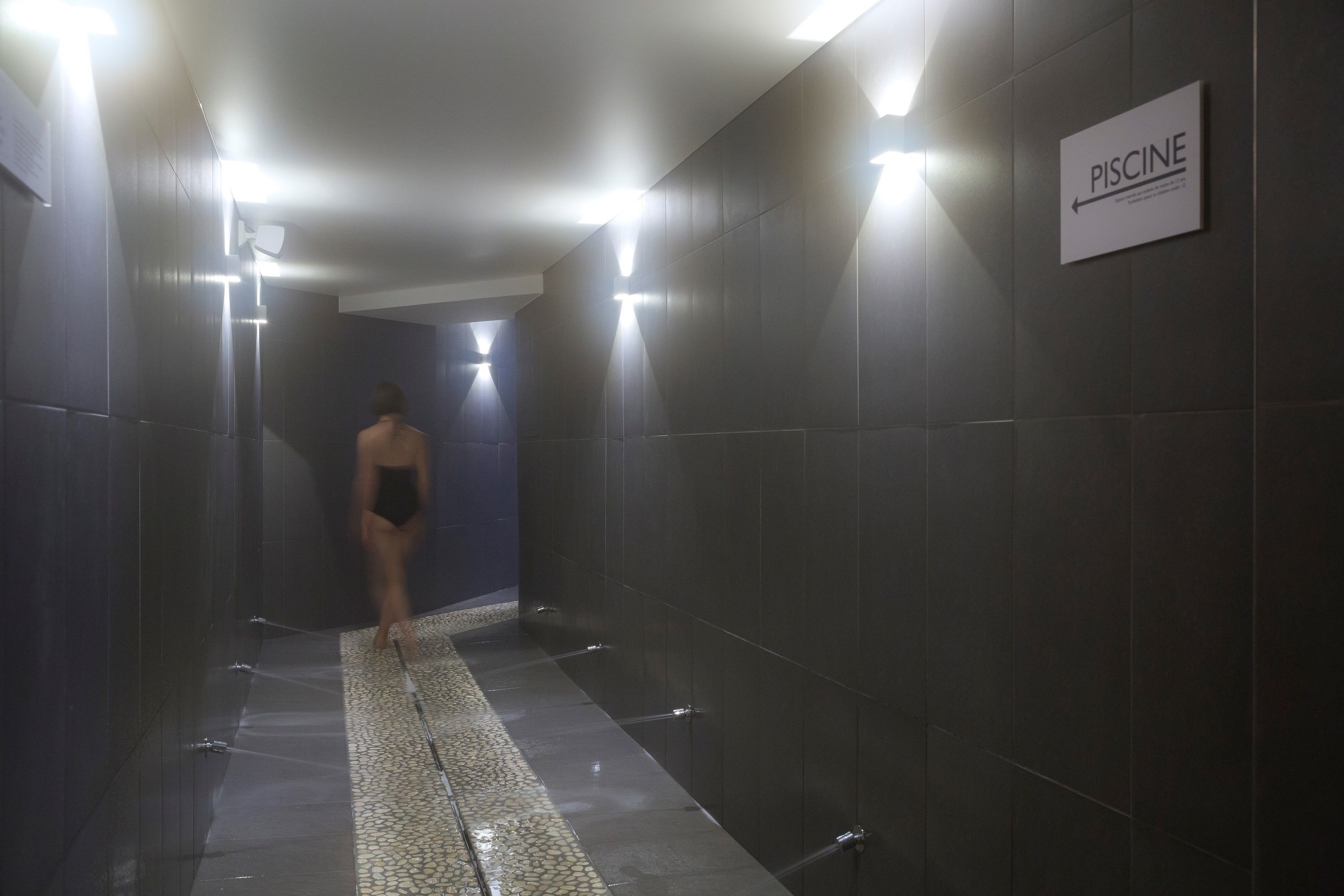 A tiled hallway with a sign indicating the direction to the PISCINE.