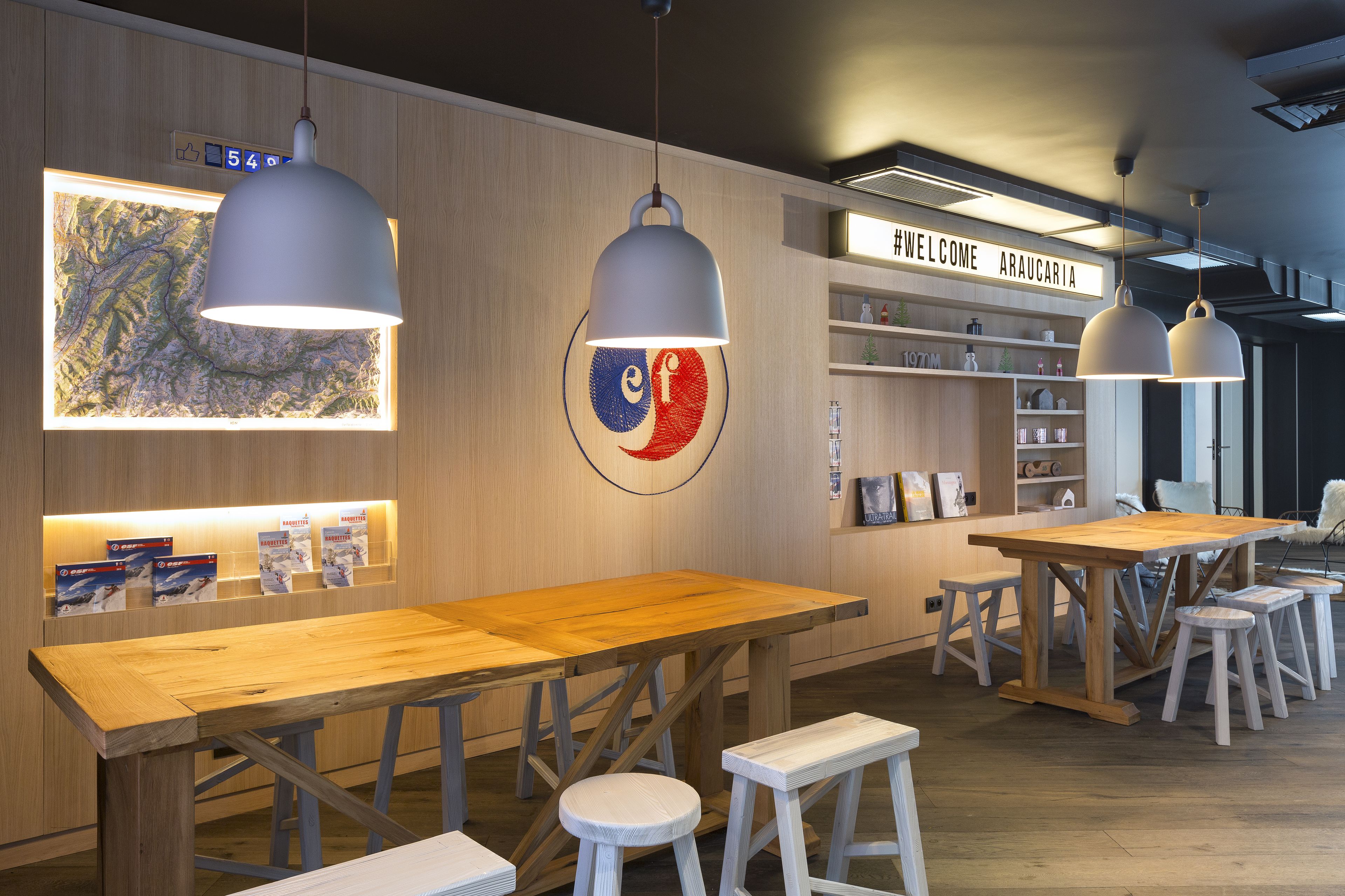 Un intérieur moderne avec des tables et des bancs en bois, une carte accrochée au mur et un panneau d’accueil.
