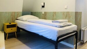A single bed with white bedding, a small yellow nightstand with a drawer, and a wall-mounted light fixture. - Hotel Damrak Inn (Amsterdam)