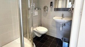 A modern bathroom with a glass shower enclosure, a toilet, and a sink. - Hotel Damrak Inn (Amsterdam)
