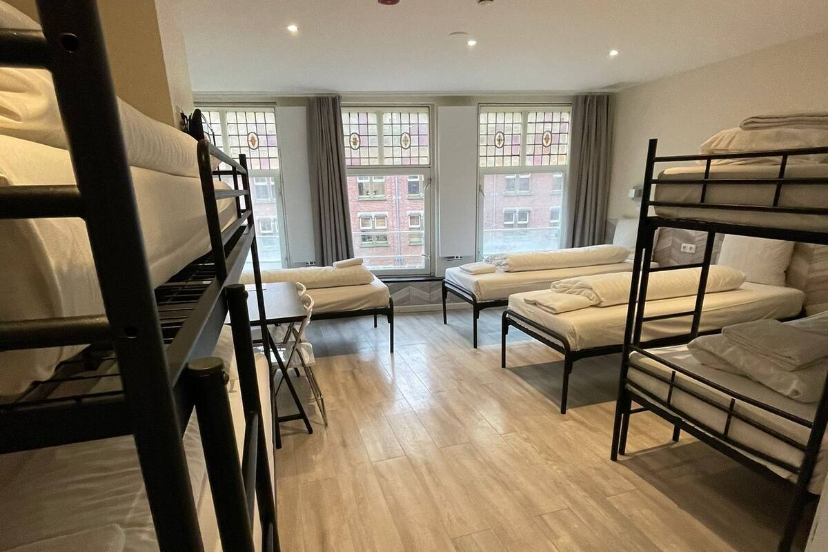 Ein Schlafsaalzimmer mit Etagenbetten, Holzboden und großen Fenstern mit Vorhängen.