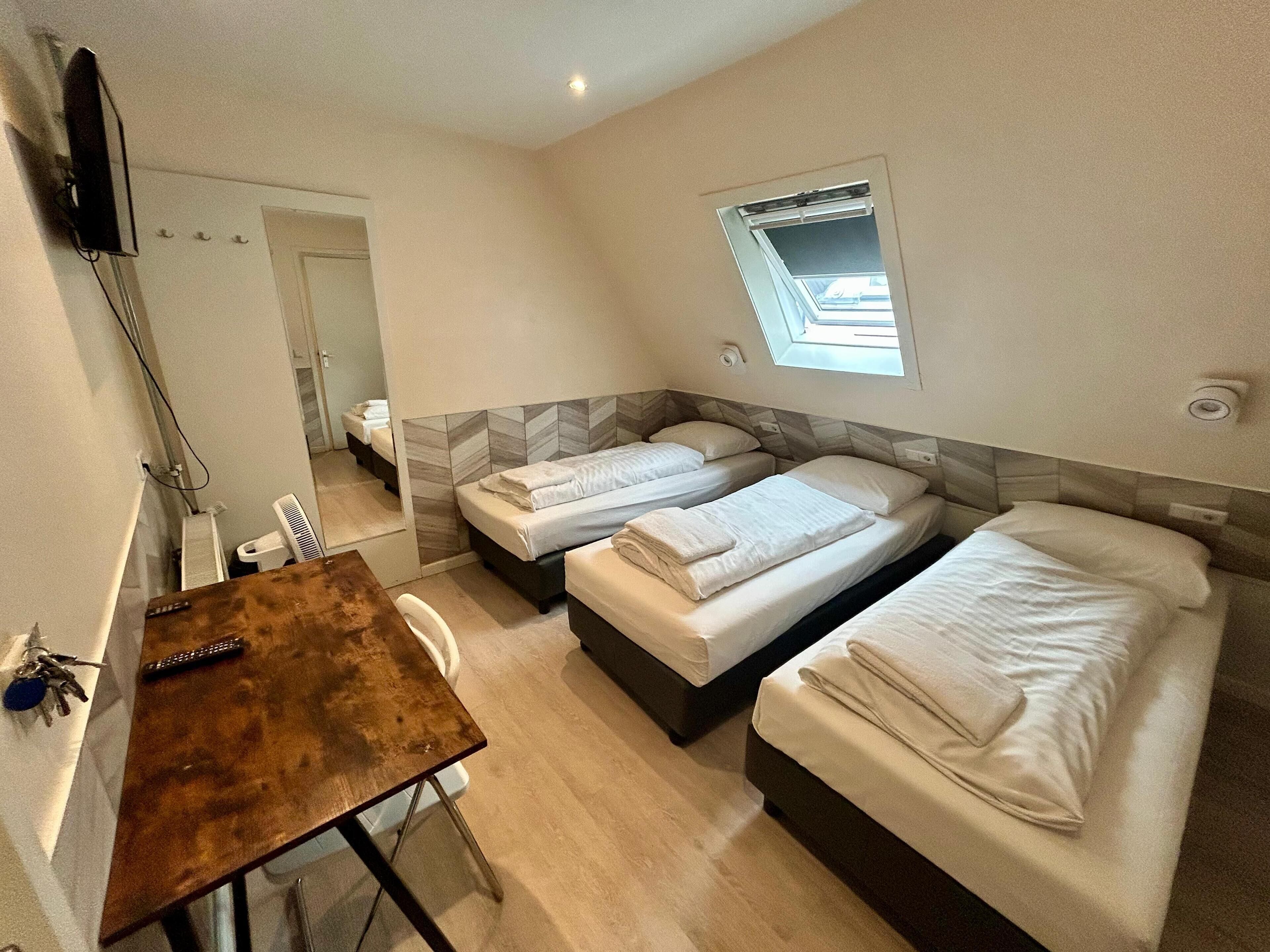 A hotel room with two single beds, a small desk, and a TV mounted on the wall.