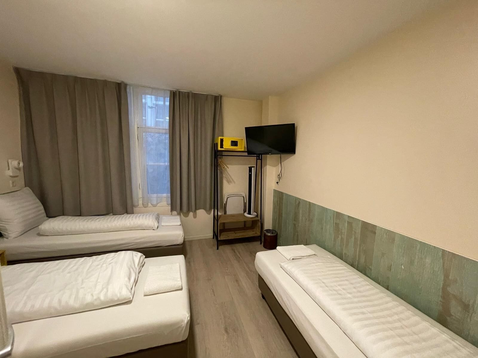 Una camera d'albergo con due letti singoli, una televisione a parete e una finestra con tende.