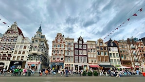 A historic European street with traditional architecture, including a prominent building with a tower and a large open square with people and shops. - Hotel Damrak Inn (Amsterdam)