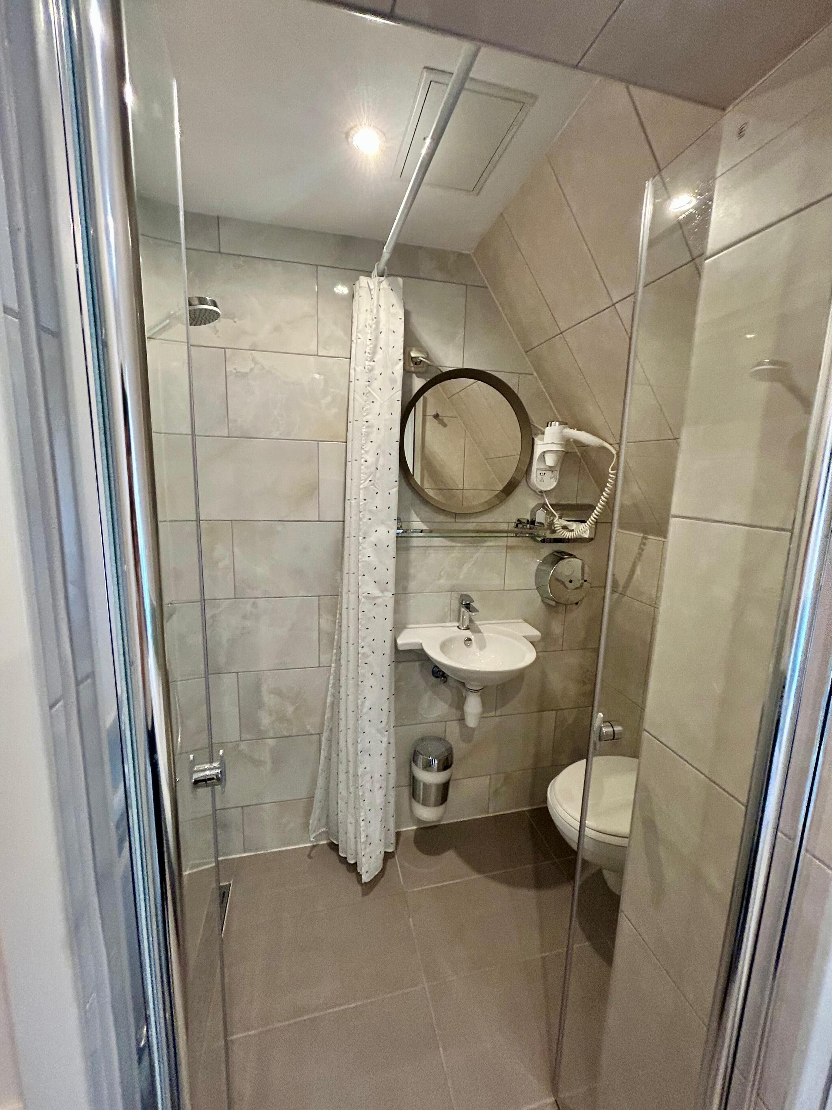 Ein Badezimmer mit Duschkabine, Waschbecken, Toilette und Spiegel.
