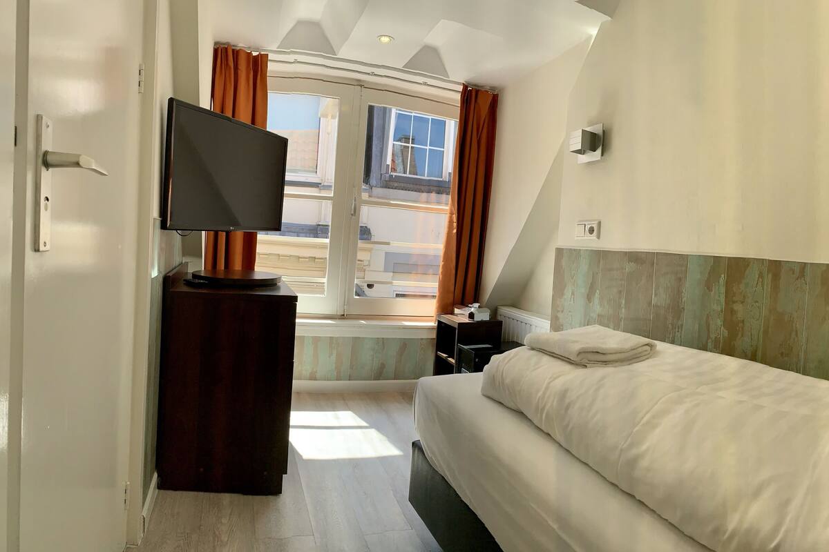 Ein Hotelzimmer mit Bett, Fernseher, einem Fenster mit Vorhängen und Blick ins Freie.