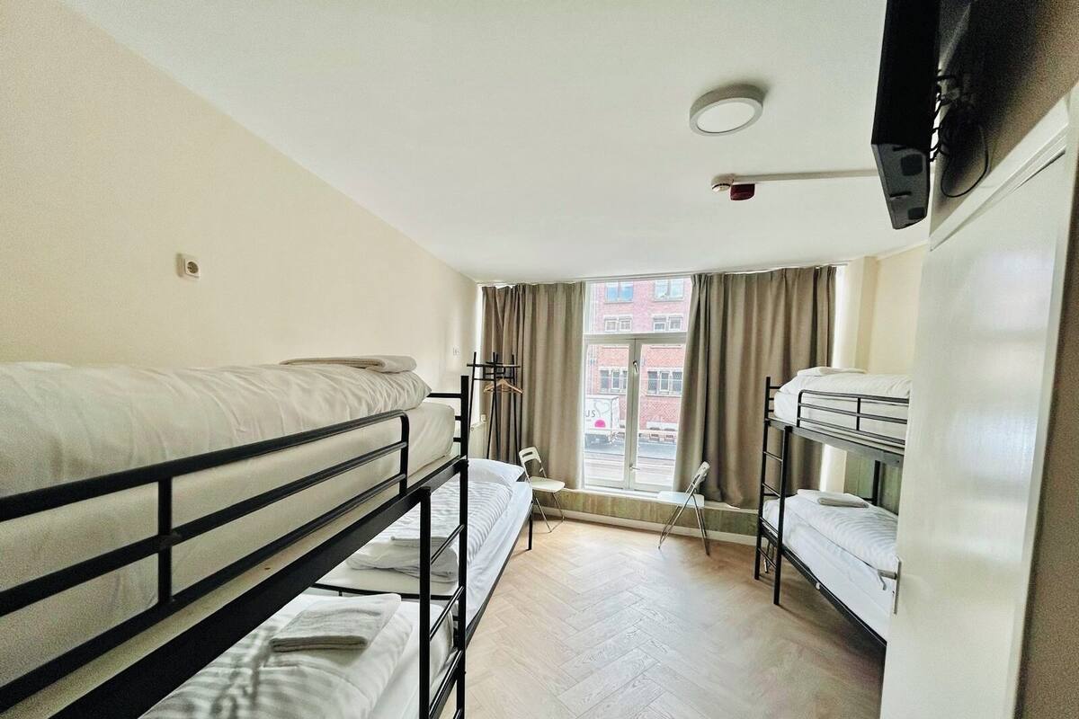 Ein Schlafsaalzimmer mit Etagenbetten, einem Fenster mit Vorhängen und einem an der Wand montierten Fernseher.