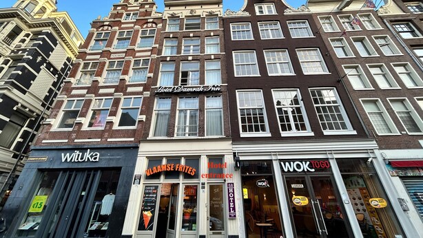 A row of European-style buildings with a variety of storefronts, including a hotel, a restaurant, and a clothing store. - Hotel Damrak Inn (Amsterdam)