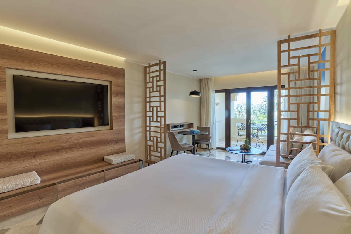 Une chambre d’hôtel moderne dotée d’un grand lit, d’un téléviseur fixé au mur, d’un bureau avec une chaise et d’un balcon offrant une vue agréable.