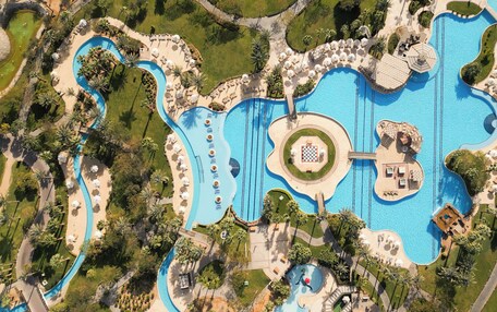 An aerial view of a resort with multiple swimming pools, sun loungers, and palm trees.