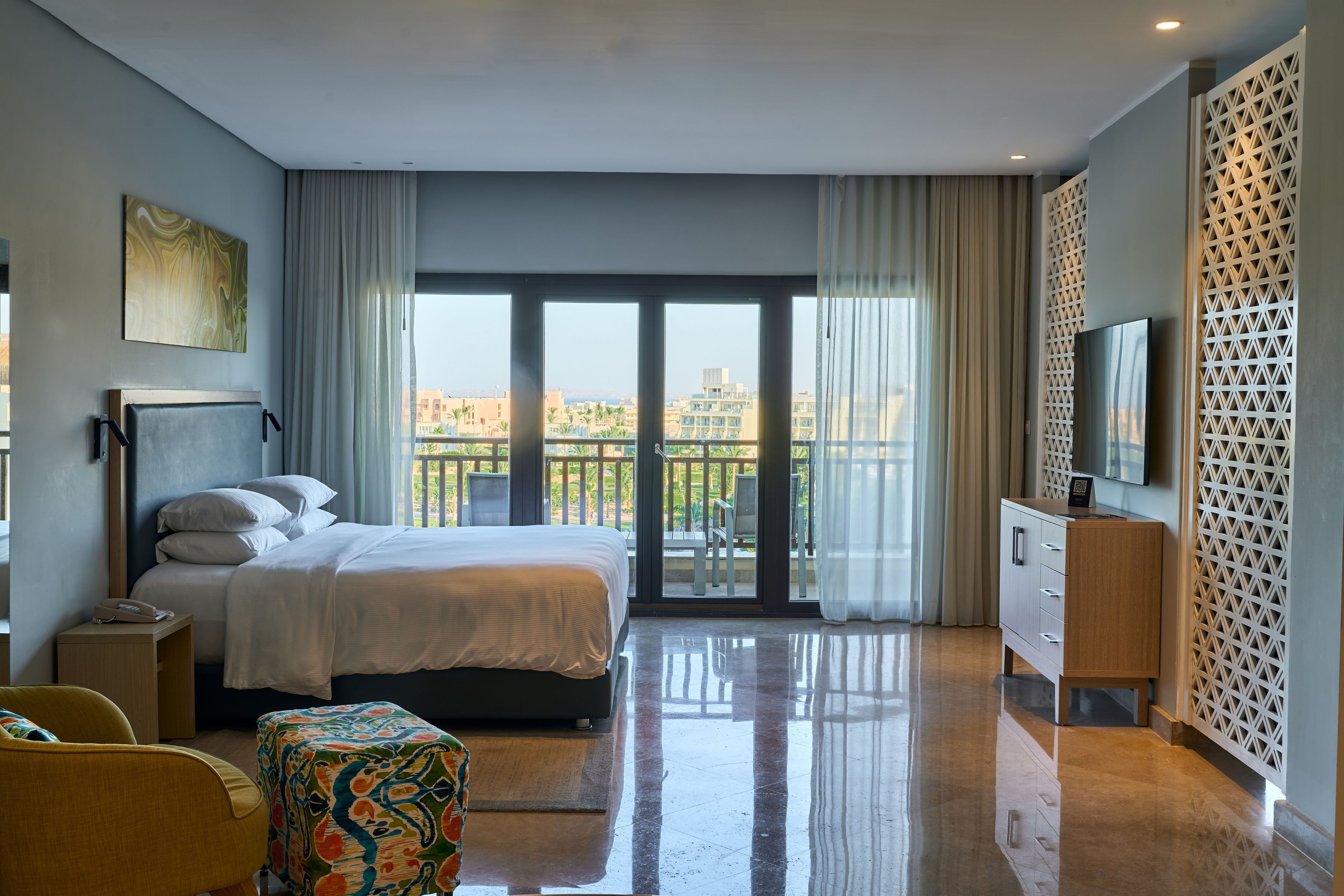 Ein modernes Hotelzimmer mit einem großen Bett, einem Fernseher, einem Schreibtisch und einem Balkon mit Blick auf die Stadt.