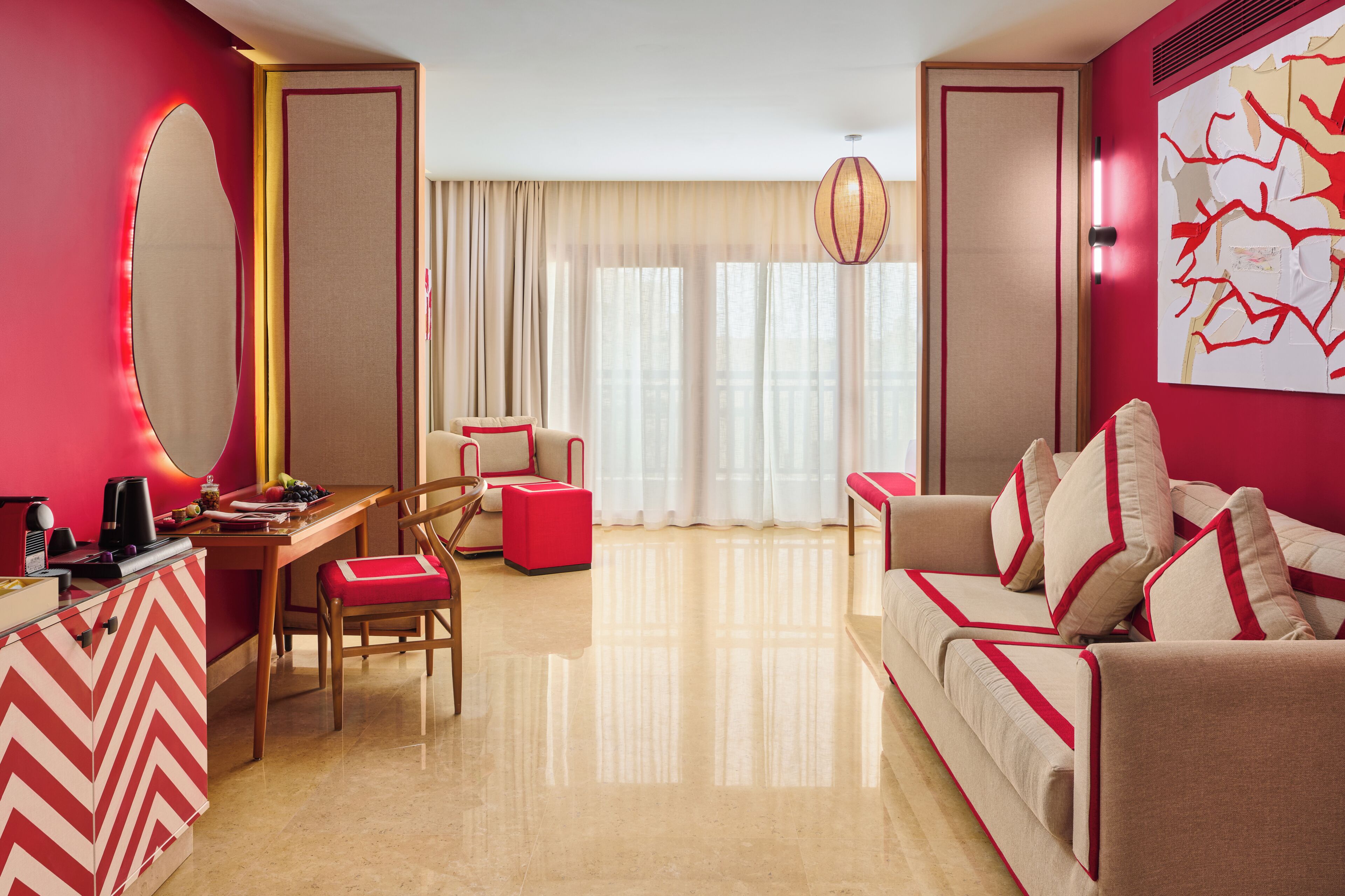 A modern hotel room with a dining area, a sofa, a desk, and a large mirror.