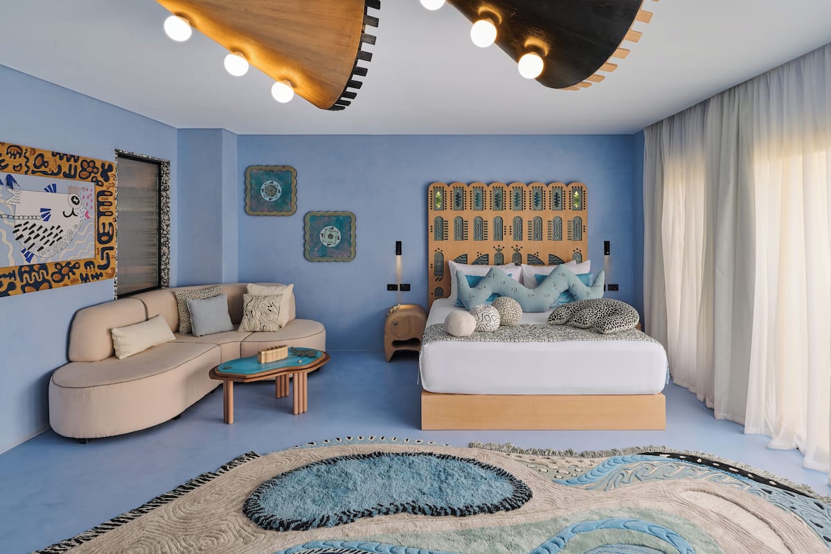 Une chambre avec un canapé, un lit, une table basse et des œuvres d’art décoratives au mur.