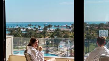 A balcony with two chairs, a small table, and a view of a resort with a pool and palm trees.