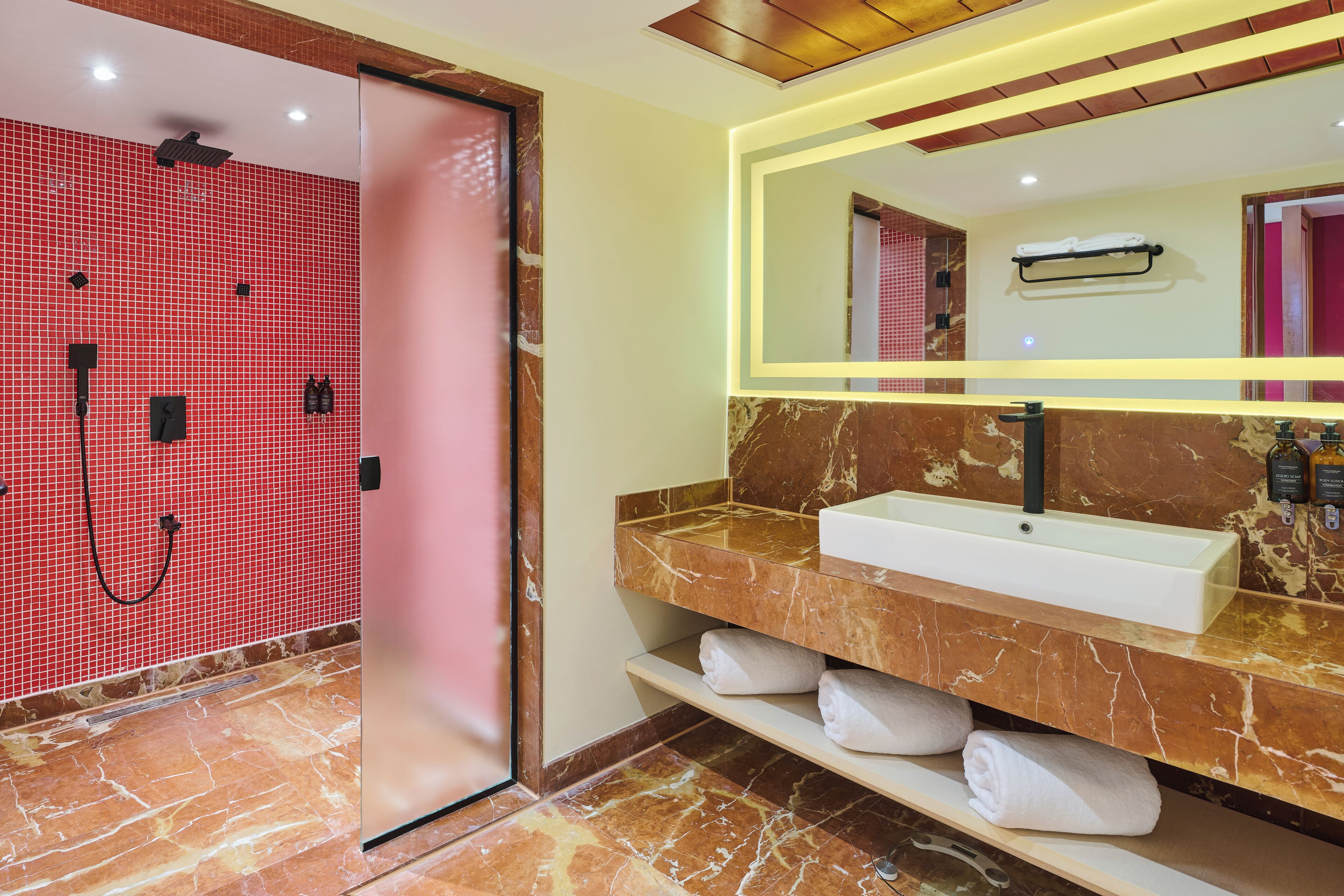 Une salle de bain moderne avec une douche dont le sol est recouvert de carreaux rouges, un meuble-lavabo en marbre et un grand miroir.