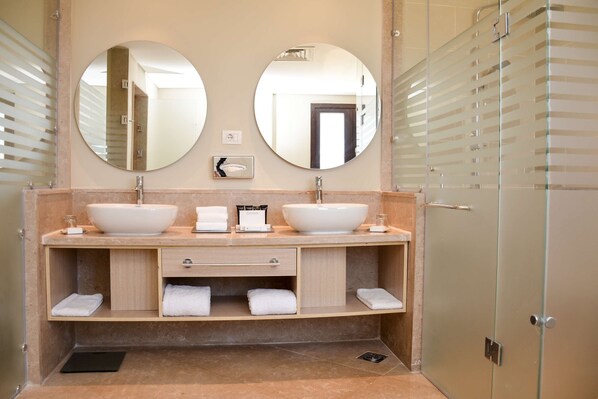 A bathroom with two large round mirrors, a double sink with a beige countertop, and a glass shower enclosure. - Steigenberger ALDAU Beach Hotel (Hurghada)