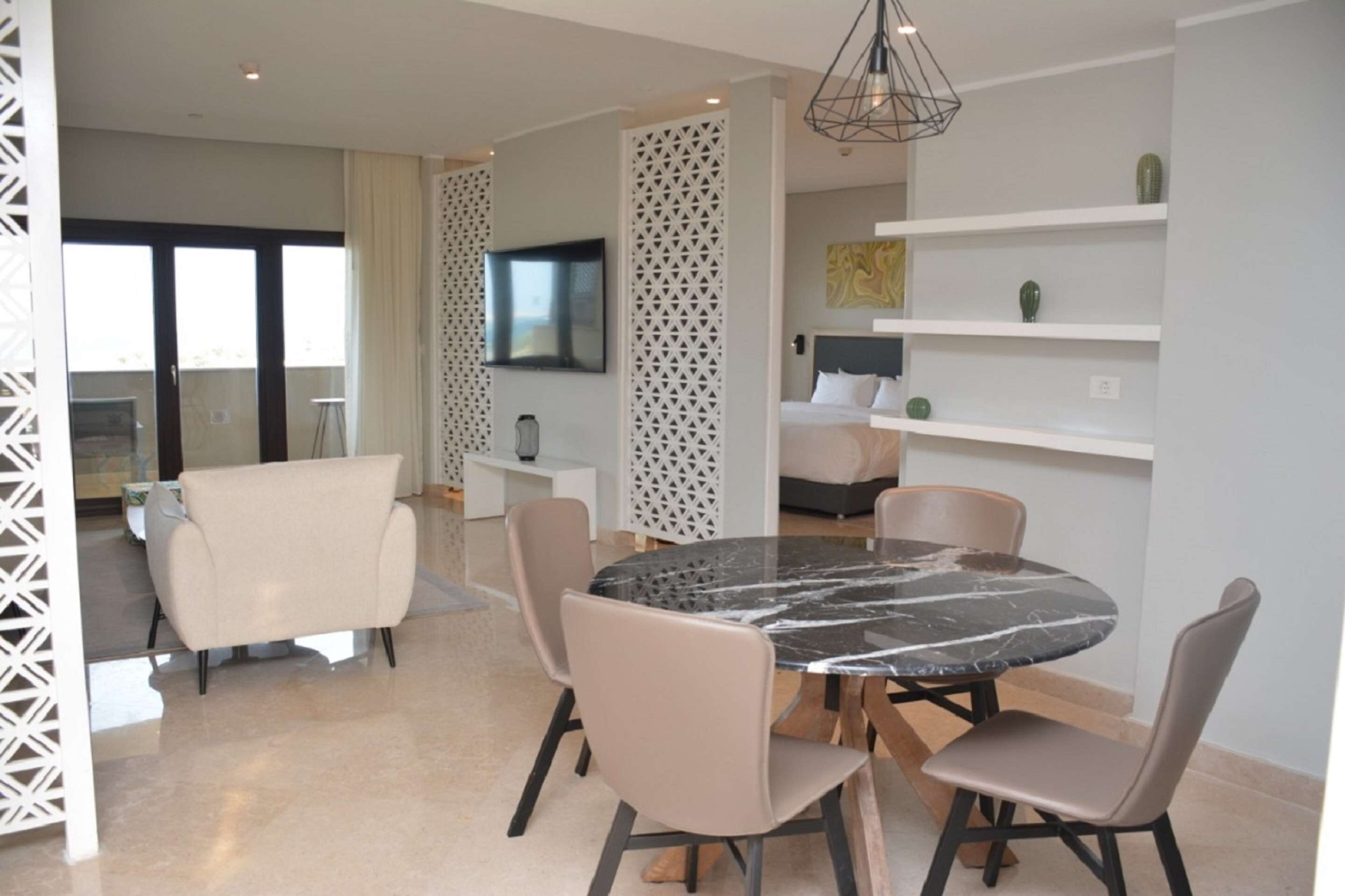 A modern dining area with a round marble table, beige chairs, and a white partition with a geometric pattern.