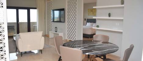 A modern dining area with a round marble table, beige chairs, and a white partition with a geometric pattern.