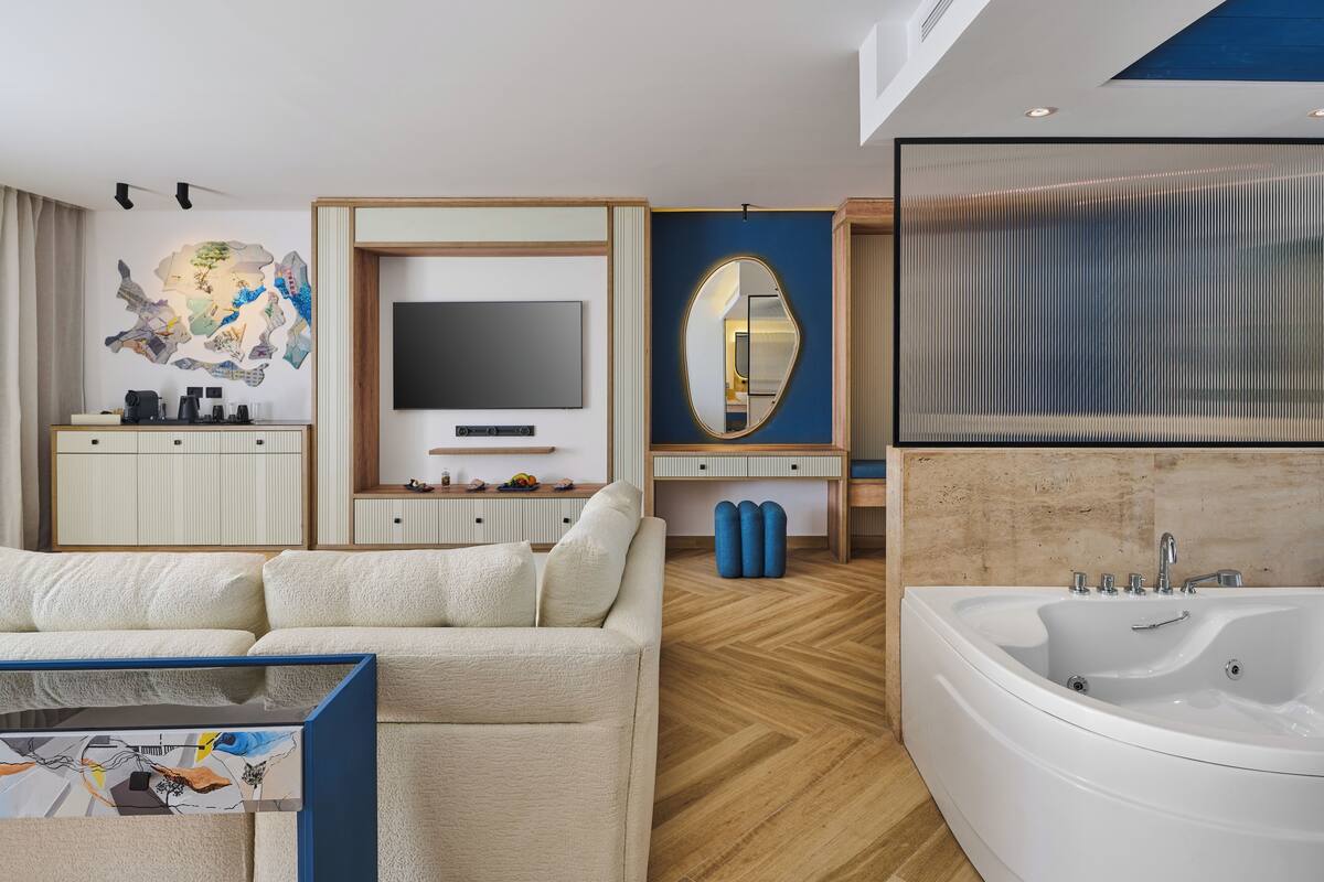 Une chambre d’hôtel moderne équipée d’un canapé, d’une télévision, d’un miroir et d’une grande baignoire.