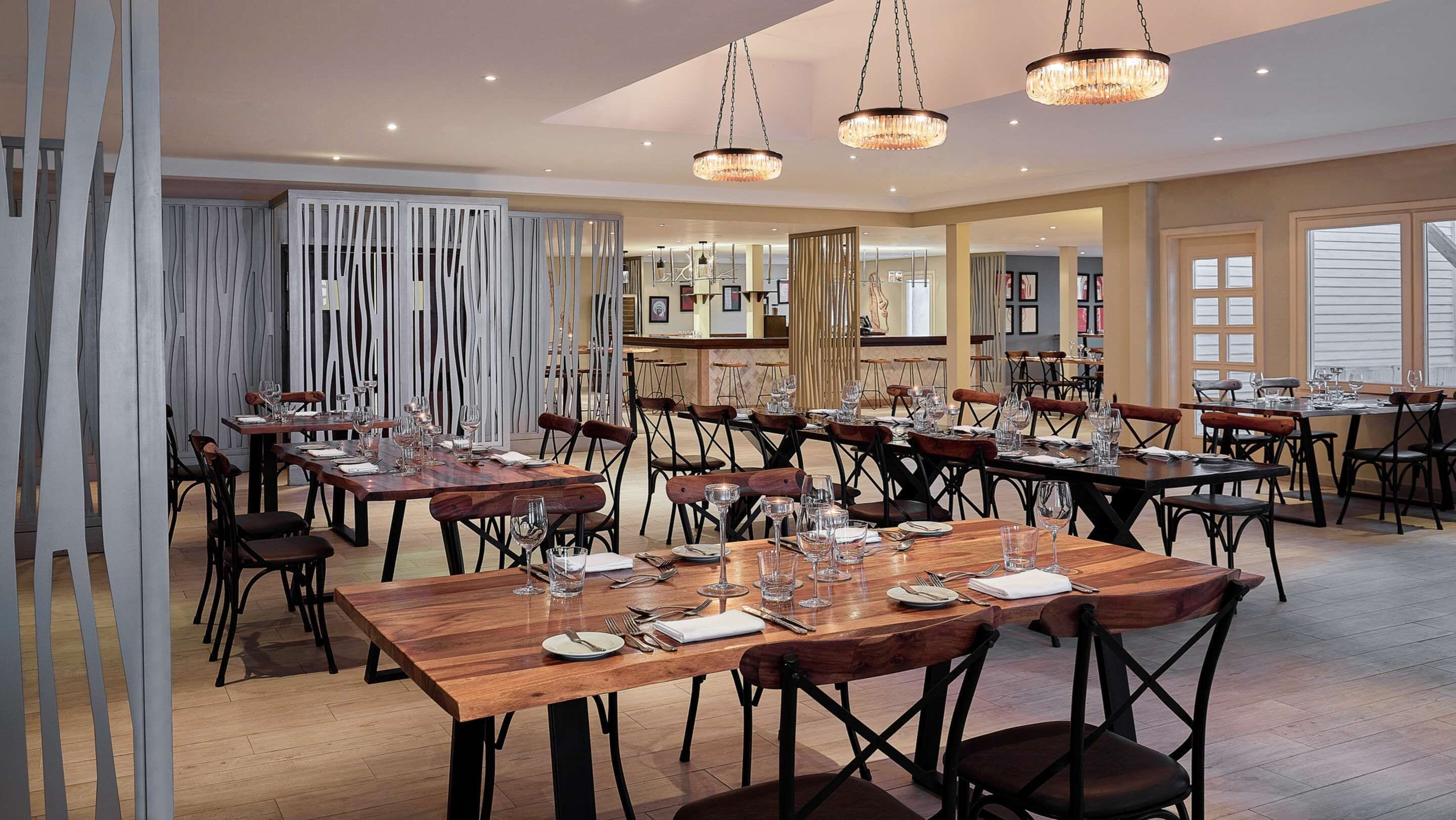 A spacious dining area with multiple tables and chairs, elegant chandeliers, and a modern interior design.