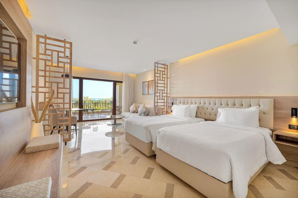 Une chambre d’hôtel avec deux lits, un balcon, un coin repas et une vue sur l’extérieur.